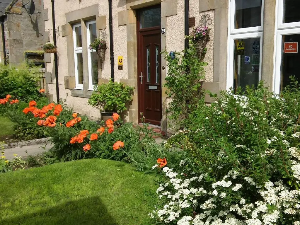 a garden with orange and white flowers in front of a house at Heathcote B&B in Inverness