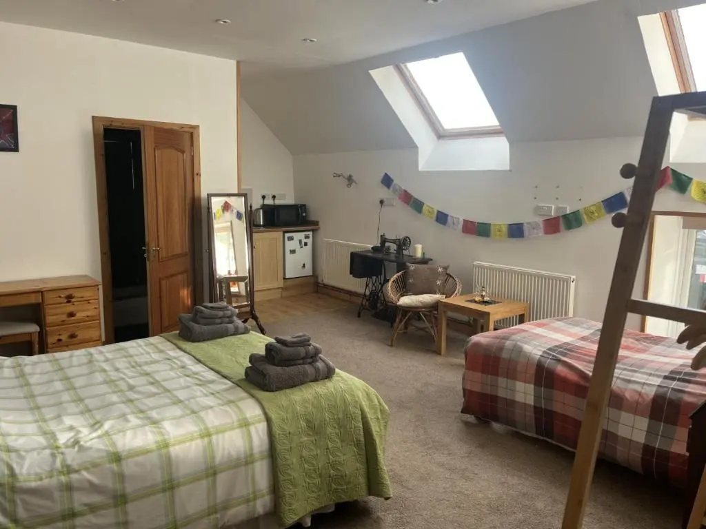 a bedroom with two beds and a table and a kitchen at Broomhead Cottages in Dufftown