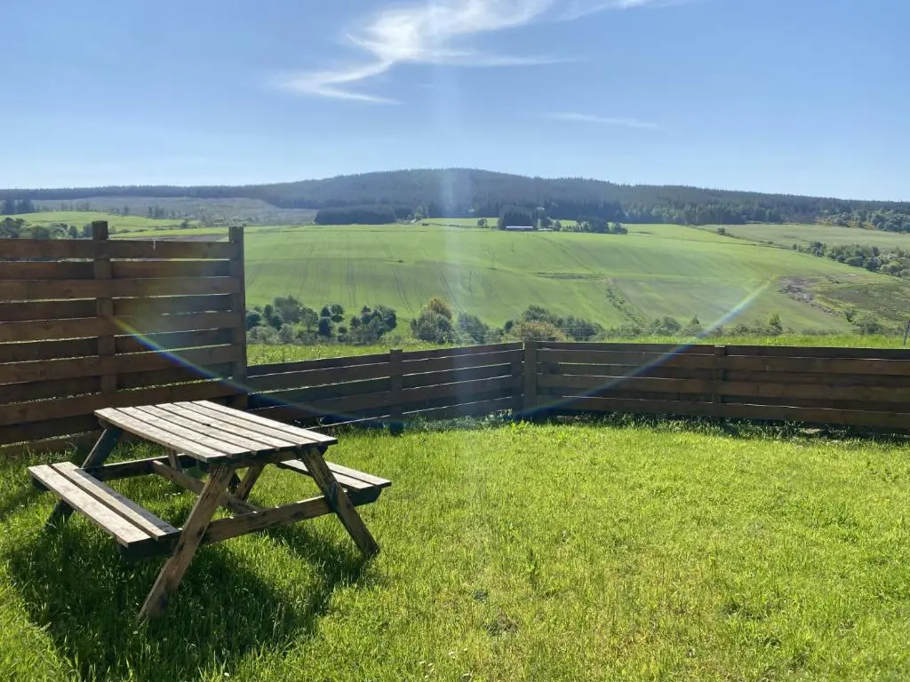 a picnic table sitting in the grass next to a fence at Broomhead Cottages in Dufftown