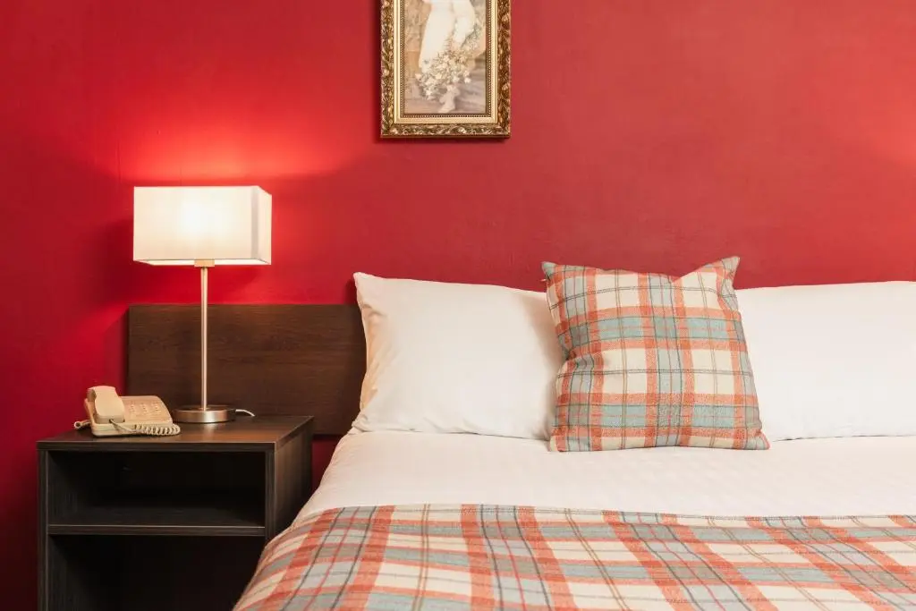 a bedroom with a red wall with a bed and a lamp at Highlander Hotel \u2018A Bespoke Hotel\u2019 in Newtonmore