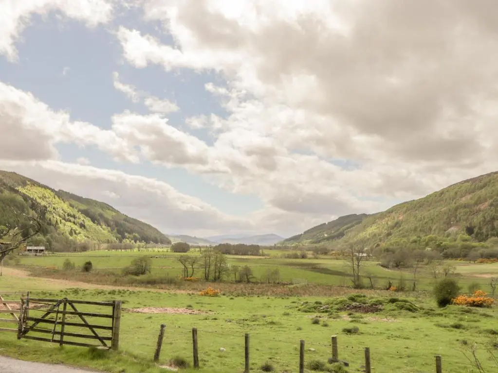 a field with a fence and mountains in the background at Crask Bungalow in Beauly