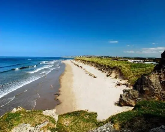 a sandy beach with people on it next to the ocean at Highway in Lossiemouth