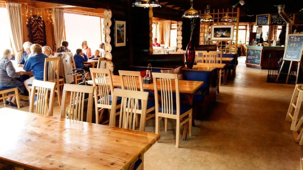 a restaurant with wooden tables and people sitting at tables at Insh Hall Rooms at Loch Insh in Kincraig