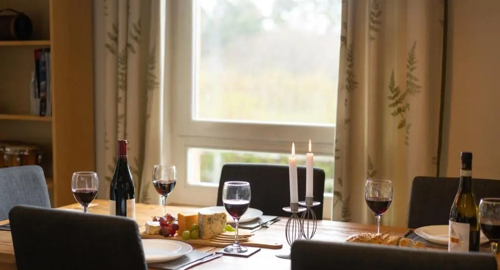a dining room table with wine glasses and a window at Salmon Run Lodge in Carrbridge