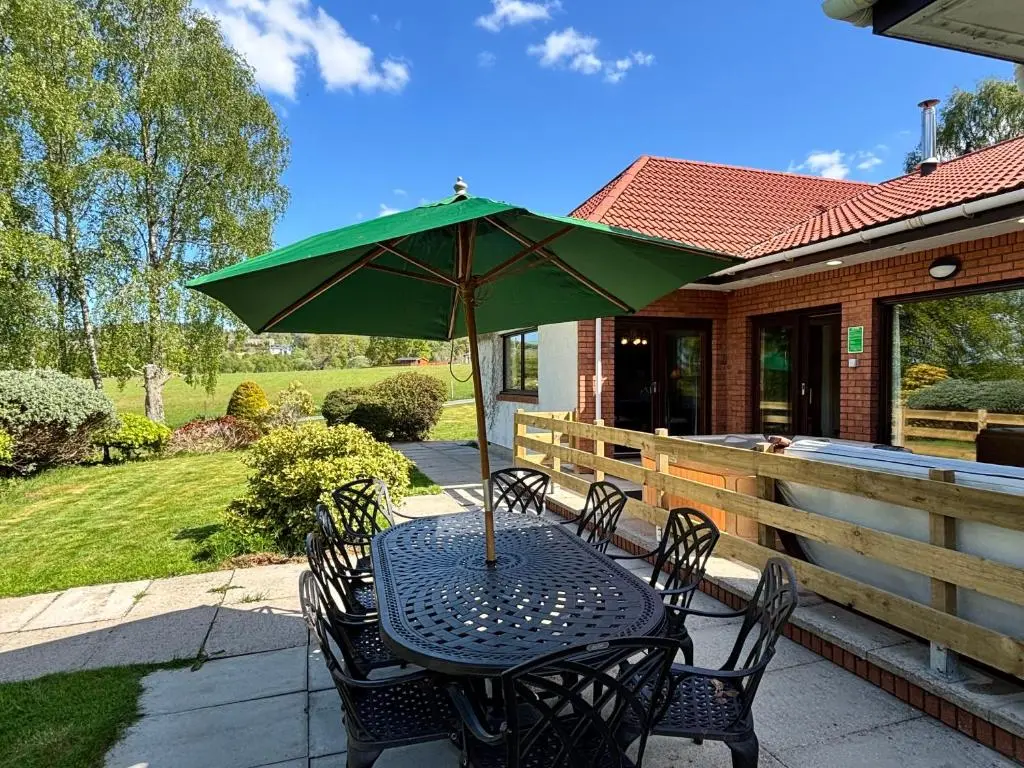 a table with a green umbrella on a patio at Corrie House with Hot Tub in Belladrum