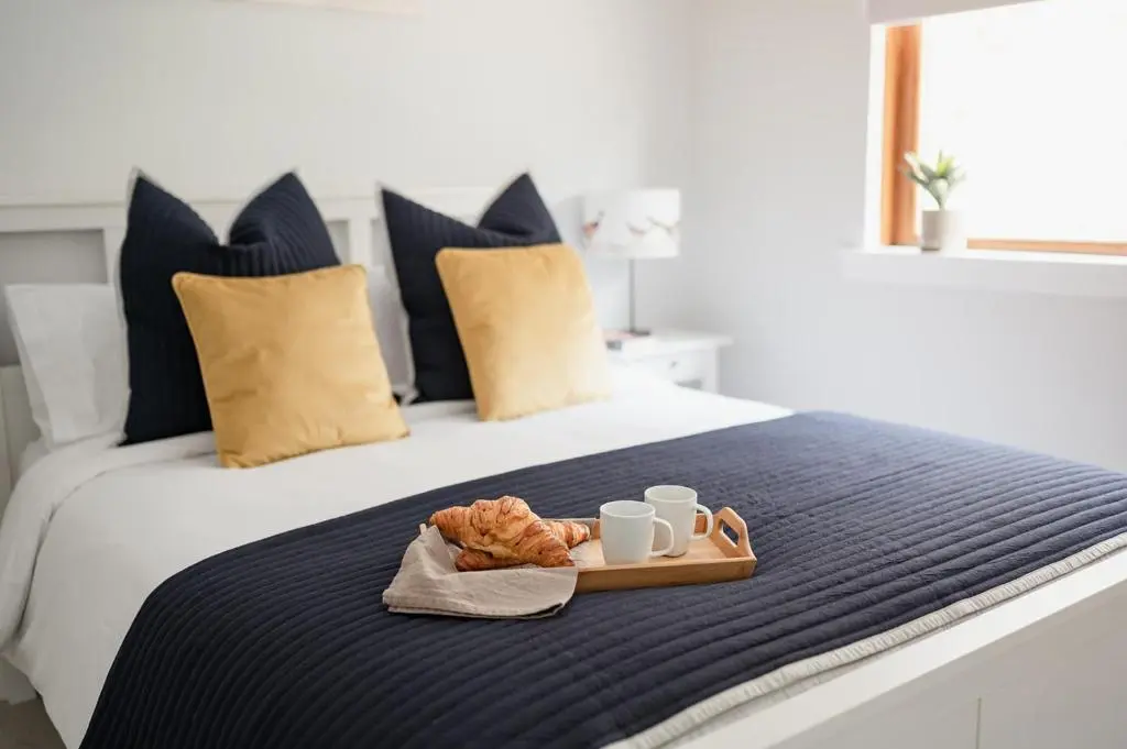 a tray of food on a bed with two mugs and croissants at Gardeners Cottage - Seasgair Lodges in Aviemore