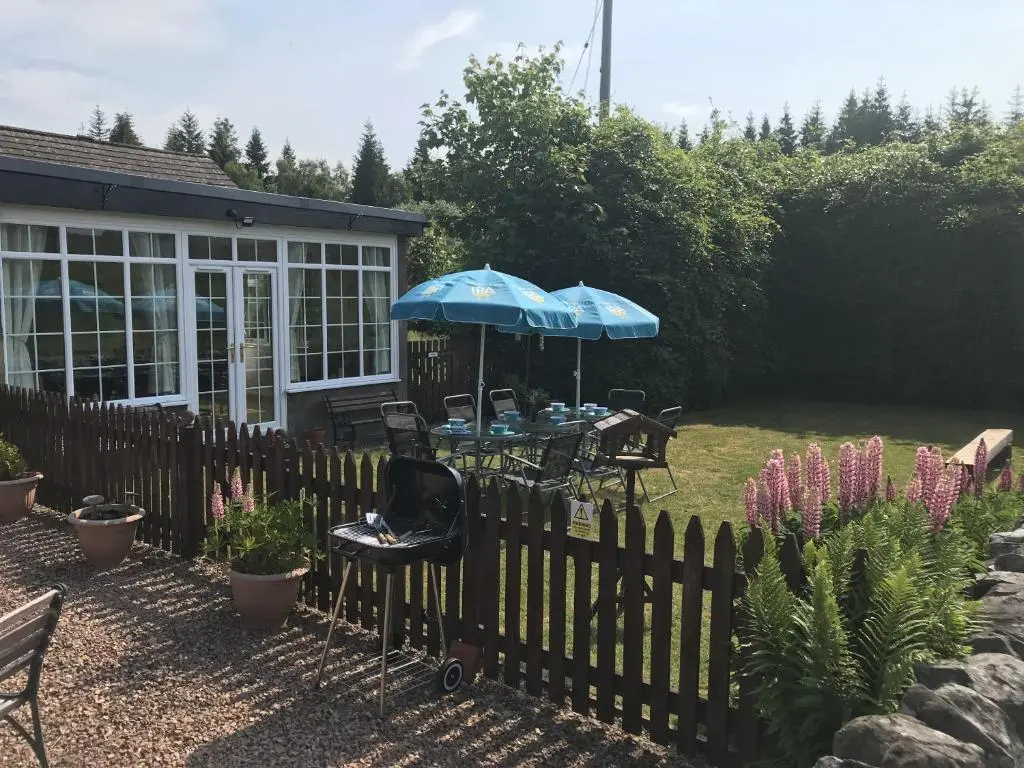 a fence with a table and umbrella in a garden at The Struan Inn Self Catering Lodge in Struan