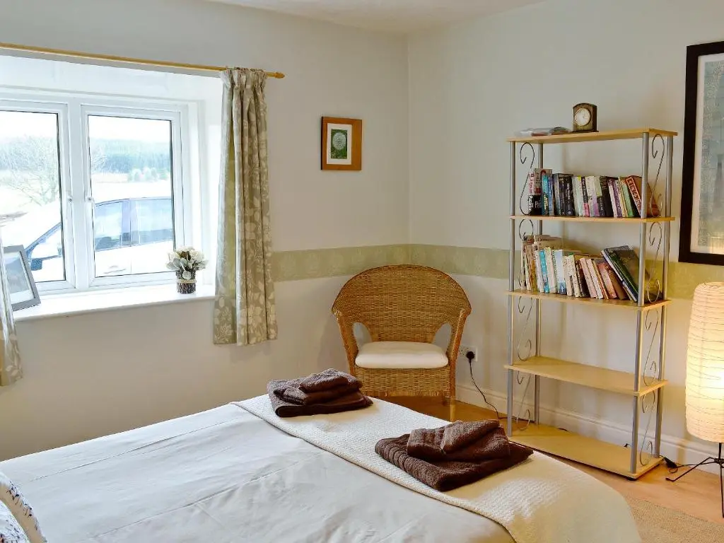 a bedroom with a bed and a chair and a window at Honey Cottage in Auchnarrow
