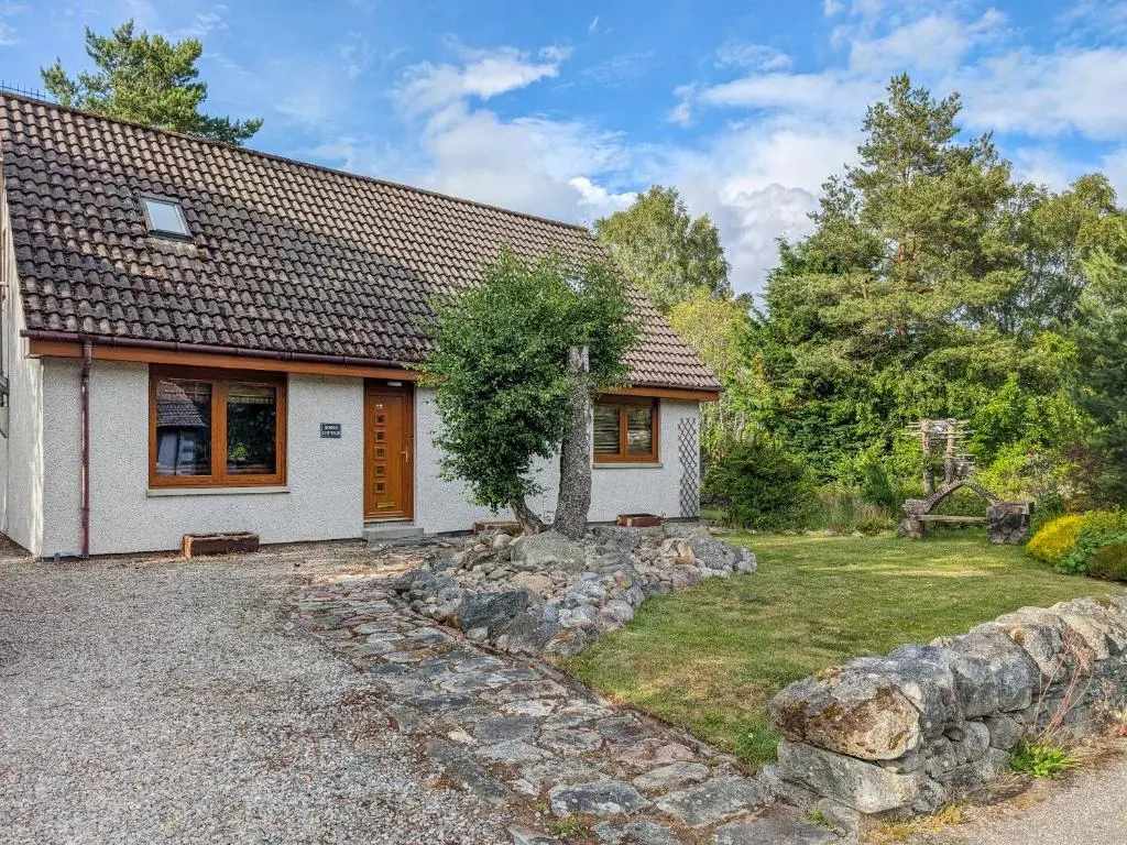 a small white house with a stone wall at Rowan Cottage in Carrbridge