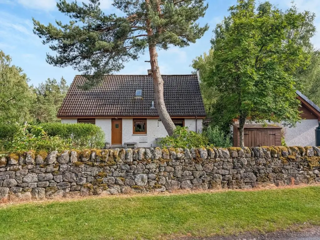 a stone retaining wall in front of a house at Rowan Cottage in Carrbridge