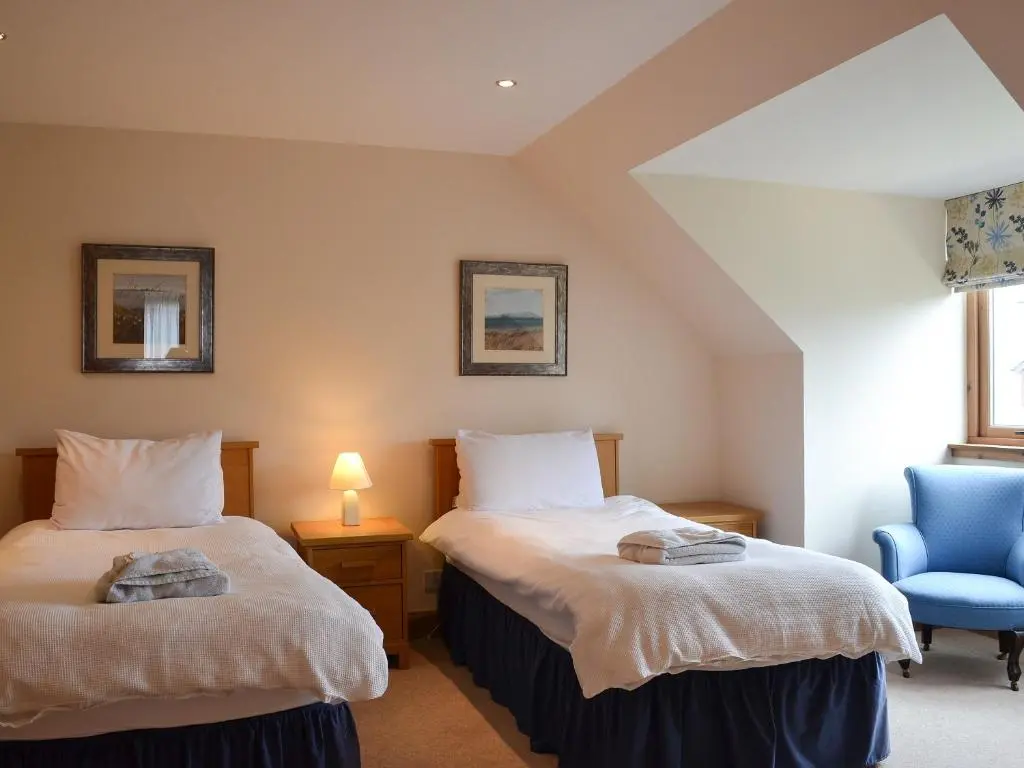 a bedroom with two beds and a blue chair at 3 Allt Mor in Aviemore