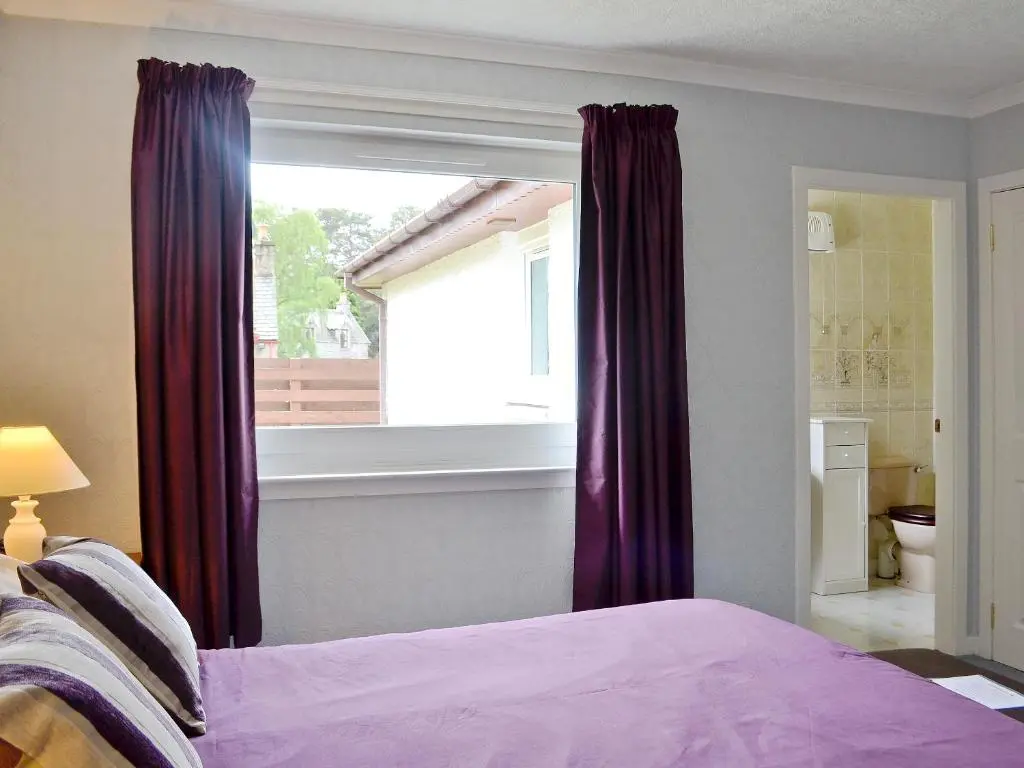 a bedroom with a bed with purple curtains and a window at Tall Pines in Carrbridge