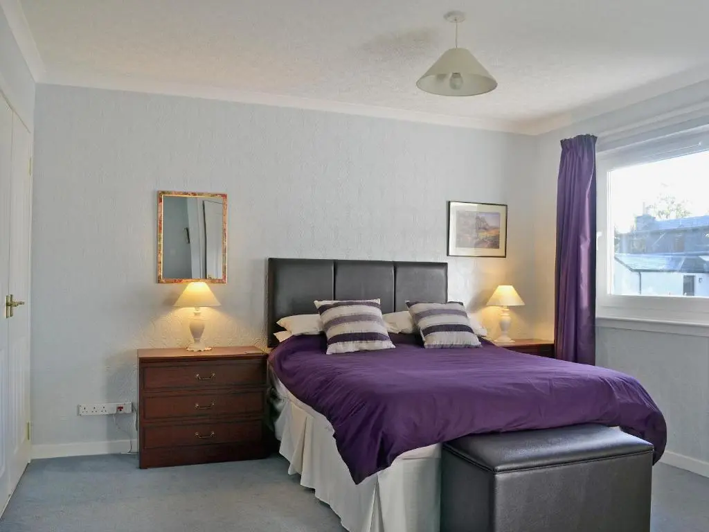 a bedroom with a bed with purple sheets and a window at Tall Pines in Carrbridge