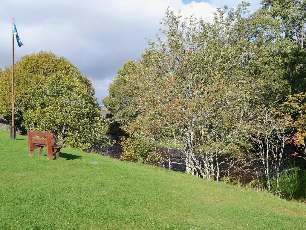 a park bench sitting on a hill next to a river at Clunymhore in Nethy Bridge