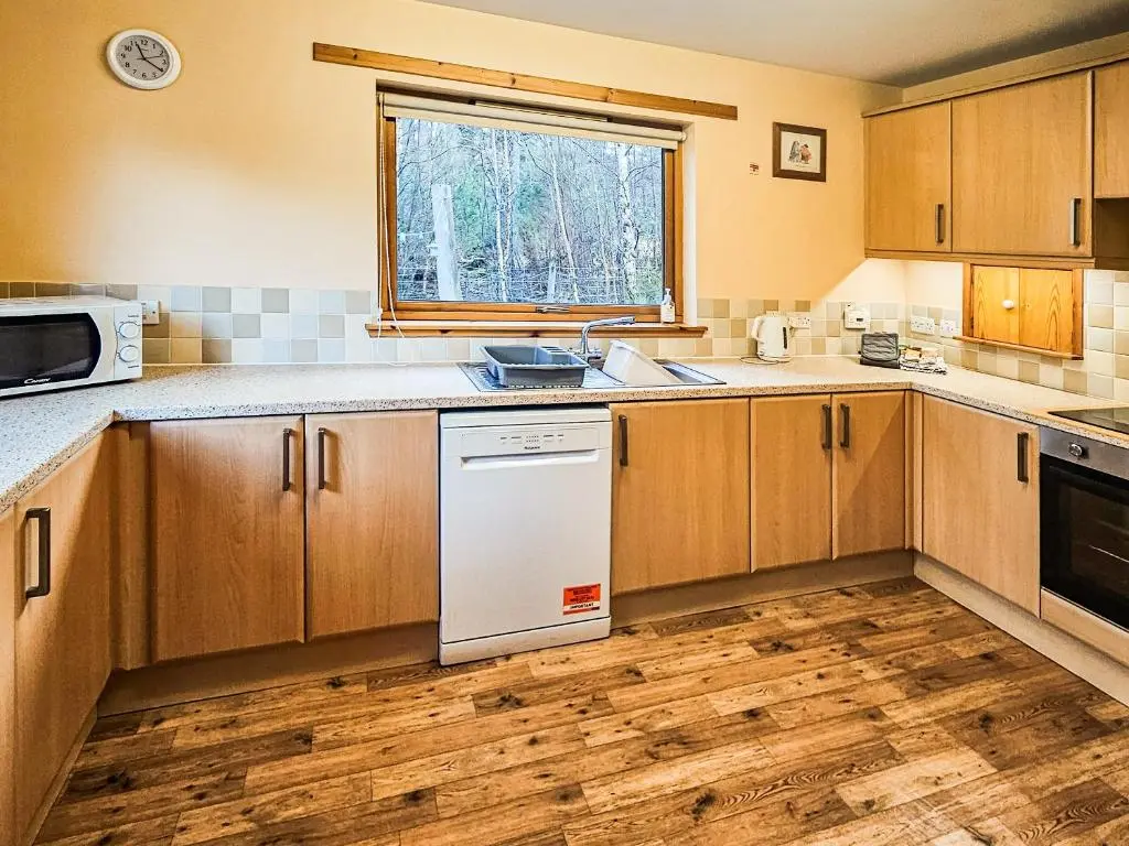 a kitchen with wooden cabinets and a white dishwasher at Clunymhore in Nethy Bridge