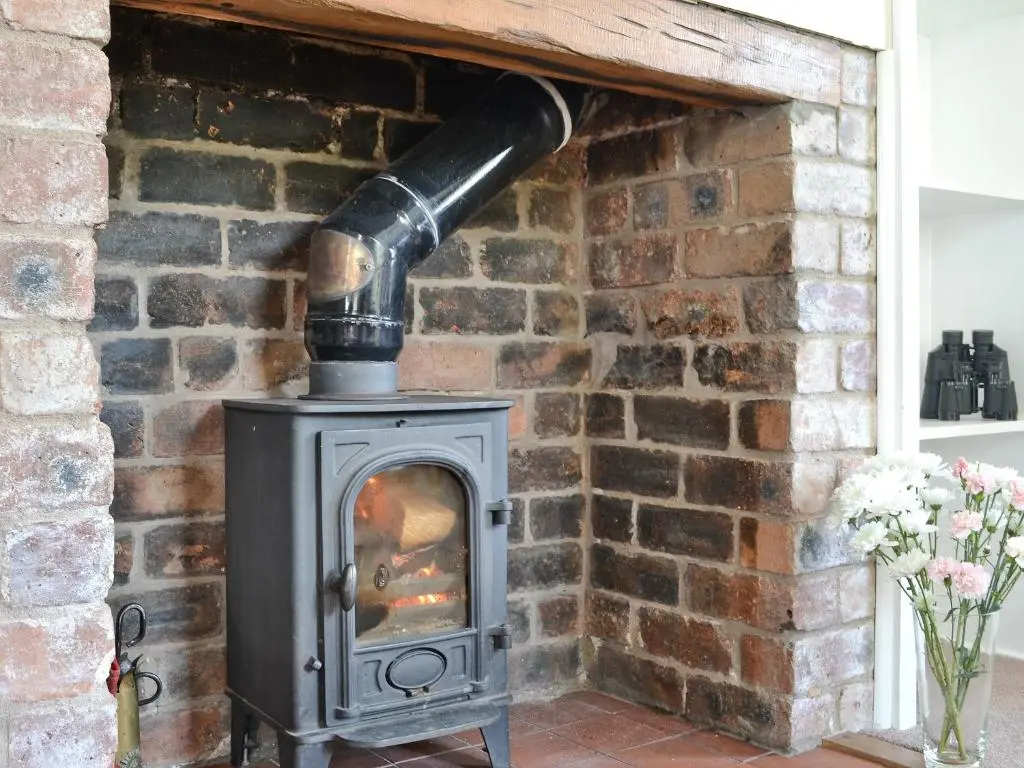 a wood stove in a brick fireplace with a pipe at Caberfeidh in Skye of Curr