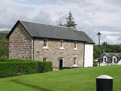 an old brick building with a black roof on a green field at Lockside Lower Flat in Fort Augustus