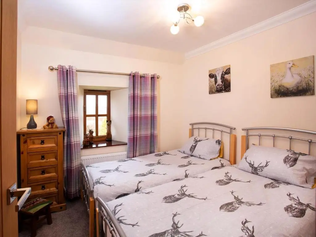 a bedroom with two beds and a dresser and a mirror at Craigellachie Cottage in Croy