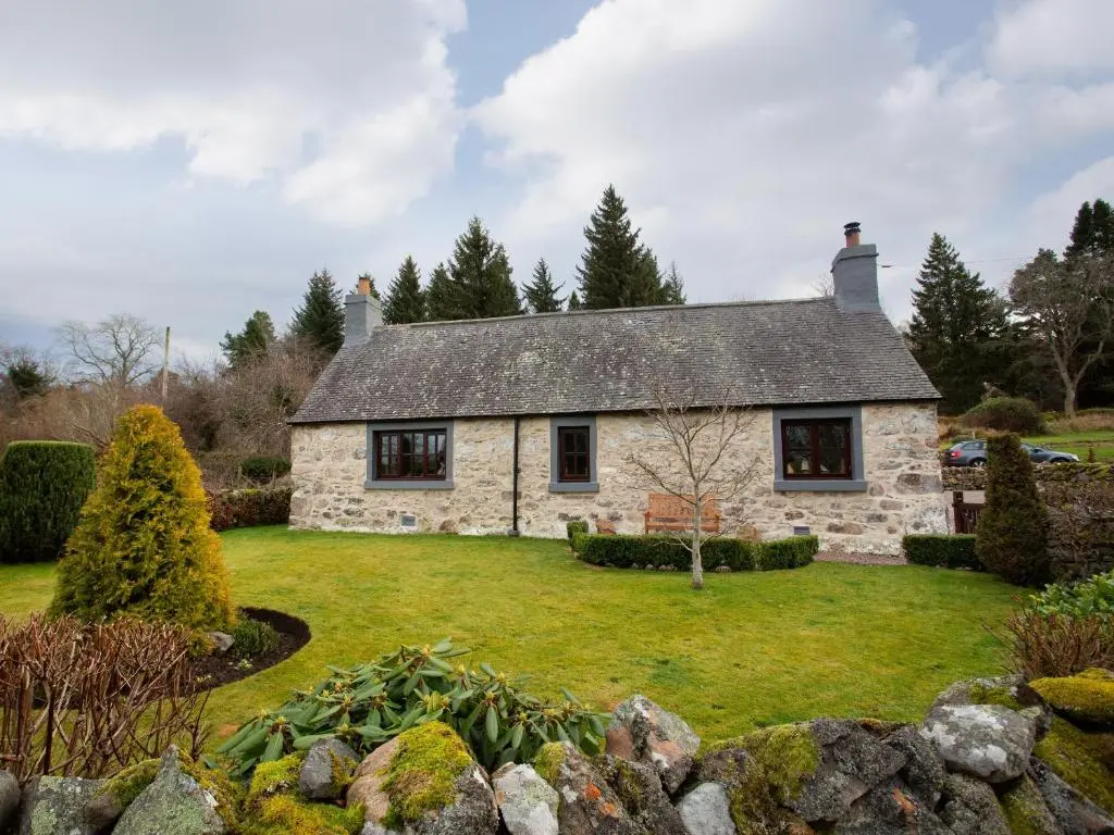 a stone house on a lawn in a garden at Craigellachie Cottage in Croy