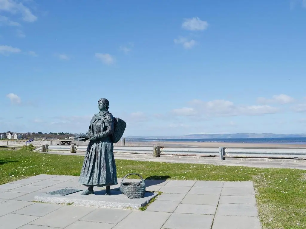 a statue of a woman standing next to the beach at Sandy Beach in Nairn