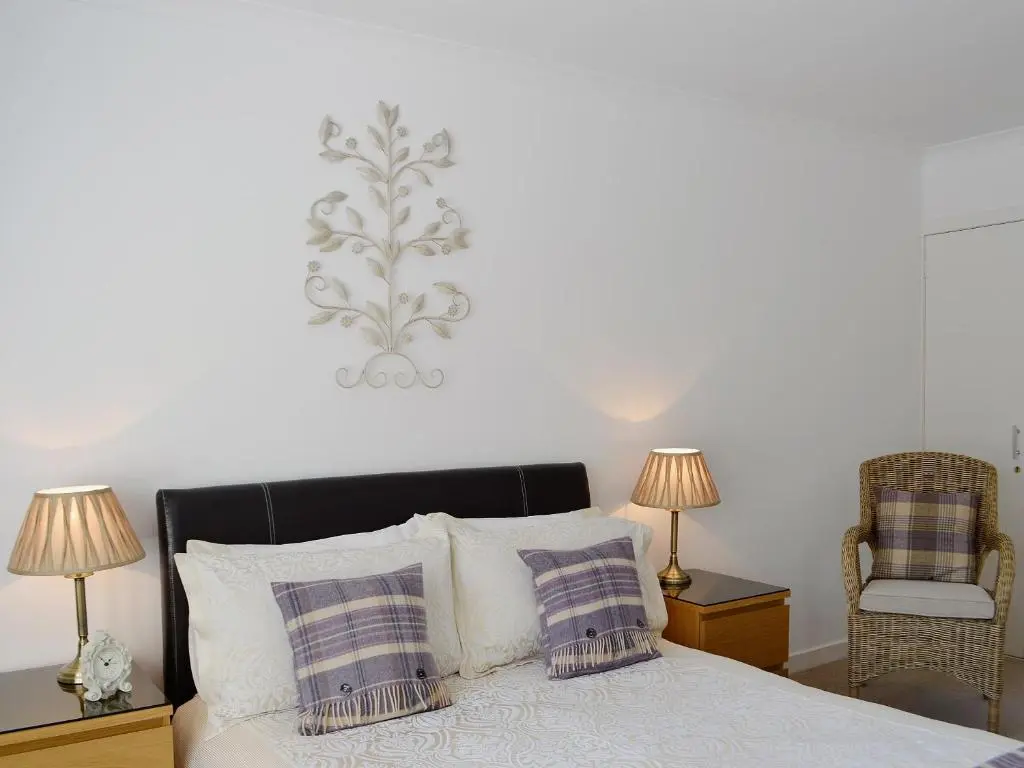 a bedroom with a bed with two lamps and a chair at Song Bird Cottage in Lochend