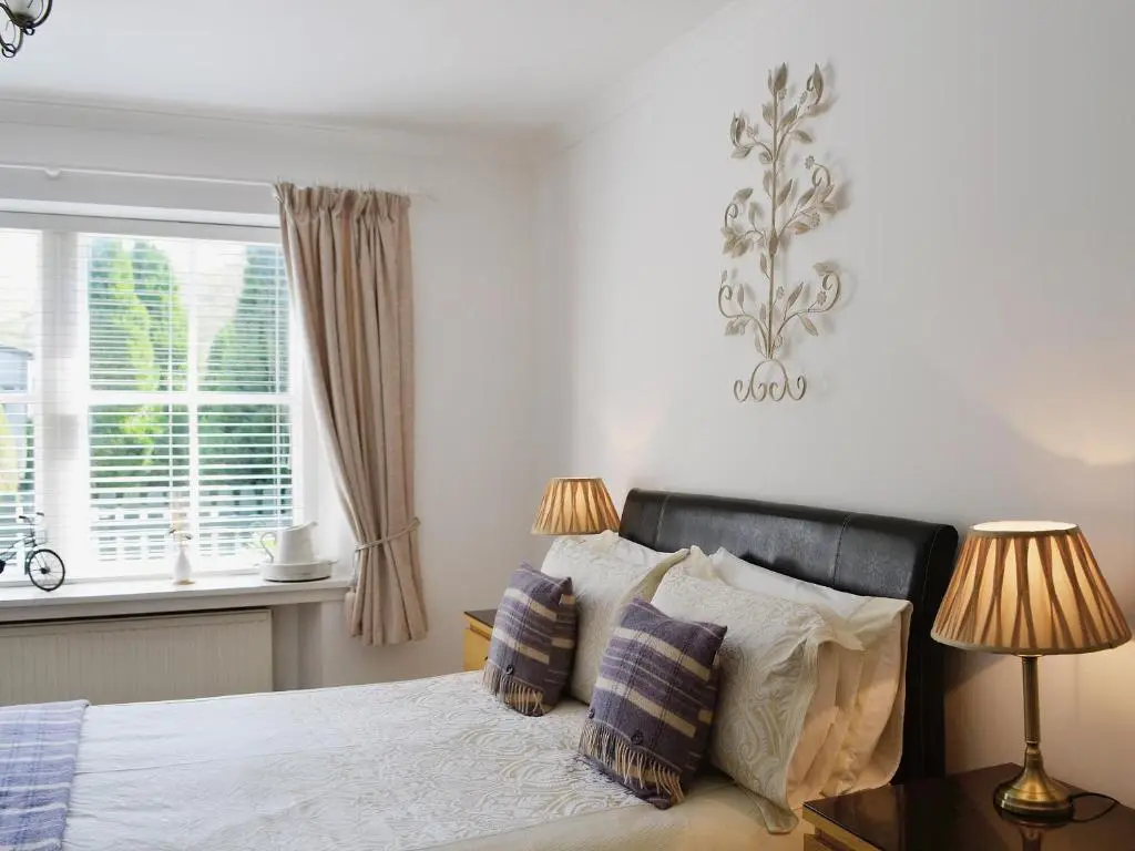 a bedroom with a bed with two lamps and a window at Song Bird Cottage in Lochend