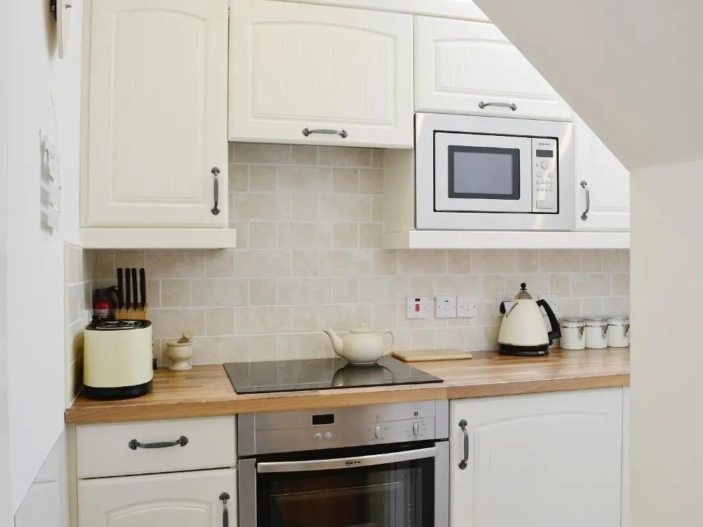 a kitchen with white cabinets and a microwave at Song Bird Cottage in Lochend