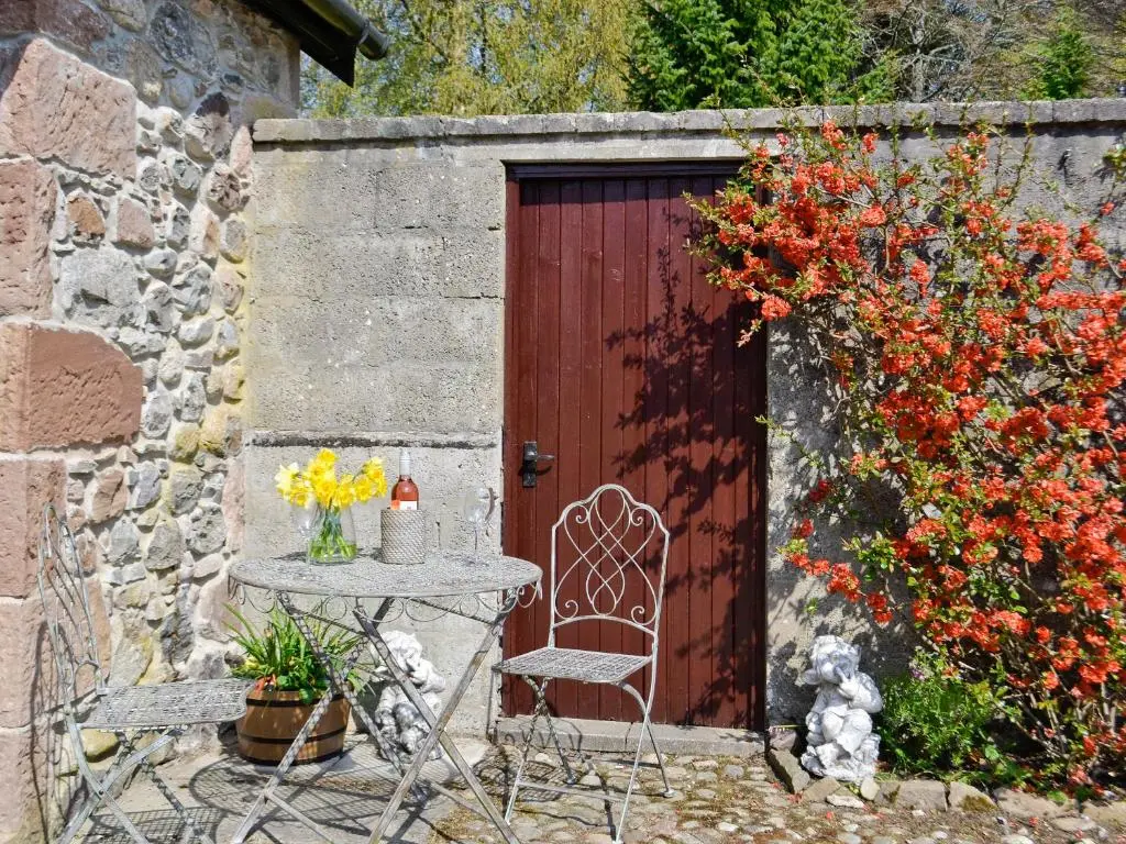 a table and chair in front of a red door at Ladybird Cottage in Lochend