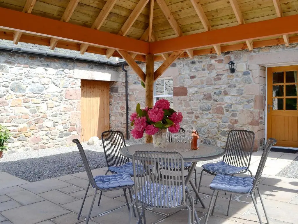 a table with chairs and flowers on a patio at Ladybird Cottage in Lochend