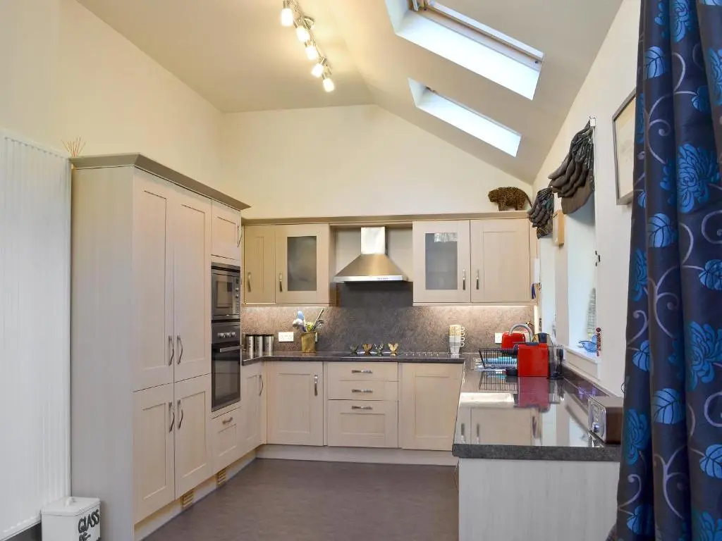 a kitchen with white cabinets and a skylight at Langside in Kingussie