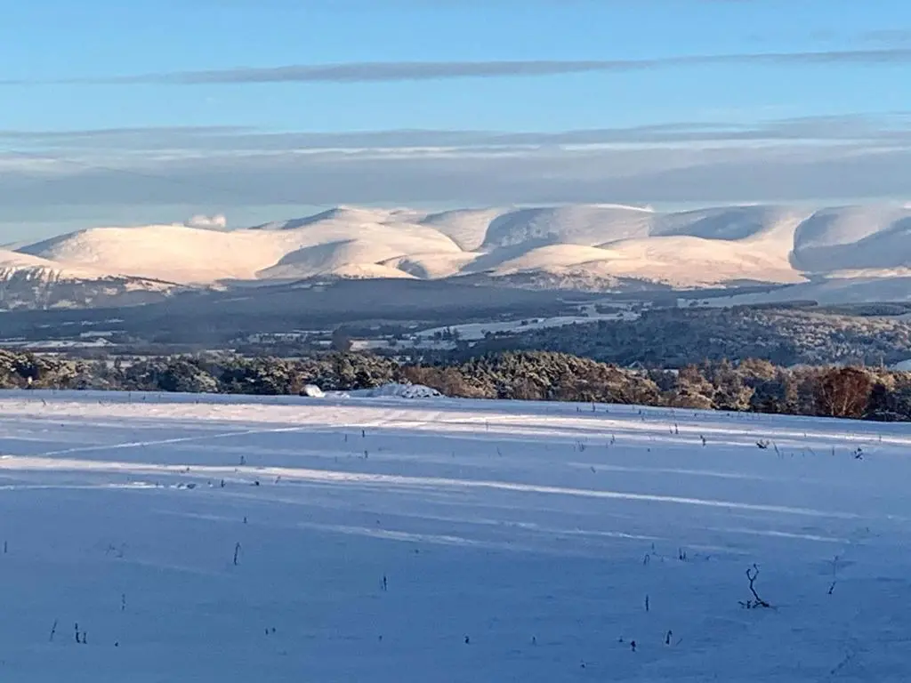 a snowy field with snow covered mountains in the background at Squirrel View in Newtonmore