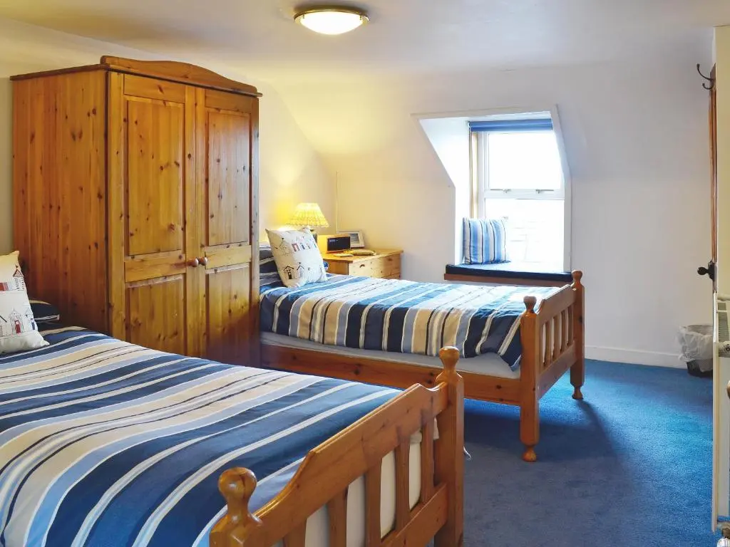a bedroom with two beds and a wooden cabinet at Boatmans Cottage - 27787 in Portessie