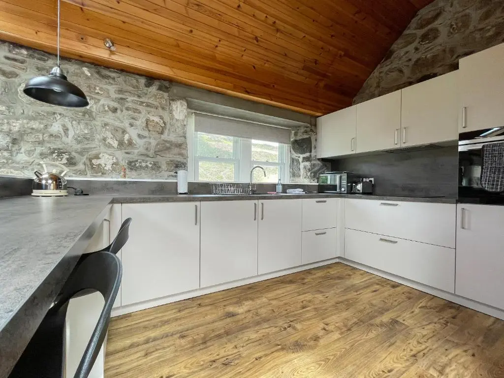 a kitchen with white cabinets and a stone wall at Glacour Studio Cottage in Bridgend