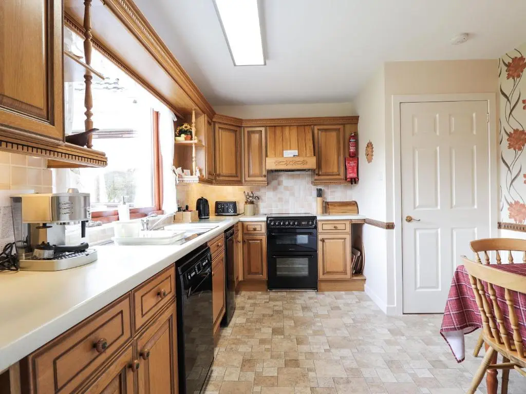 a kitchen with wooden cabinets and a sink and a stove at Holly Cottage in Gorstan