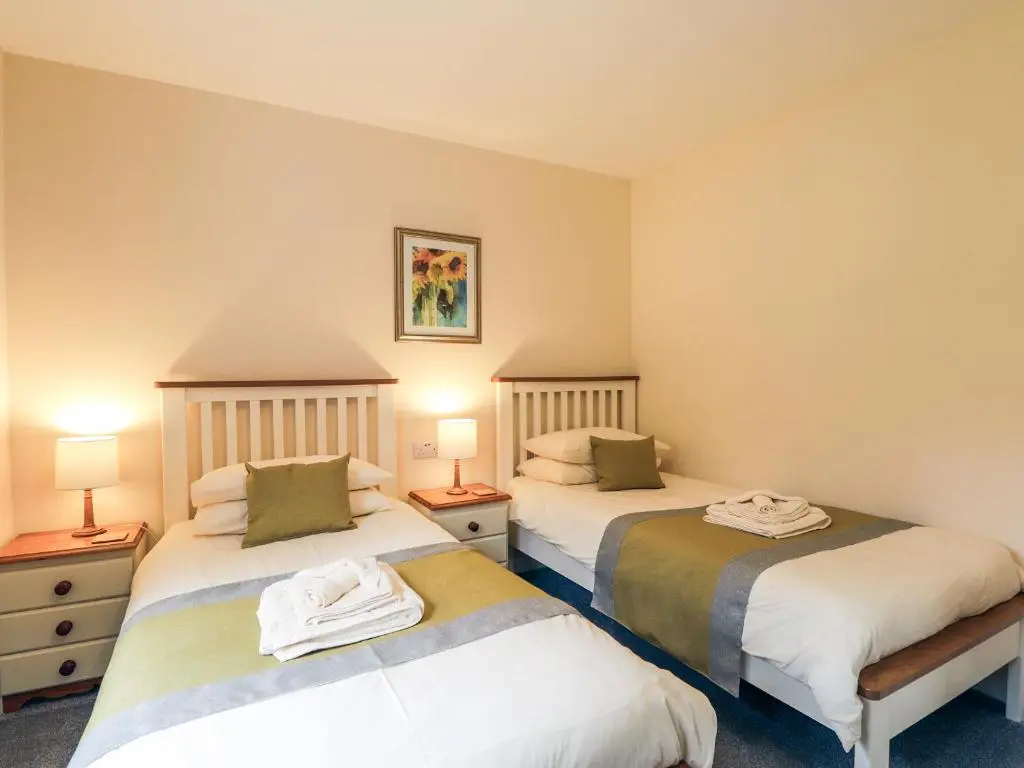two beds in a room with two lamps at Holly Cottage in Gorstan