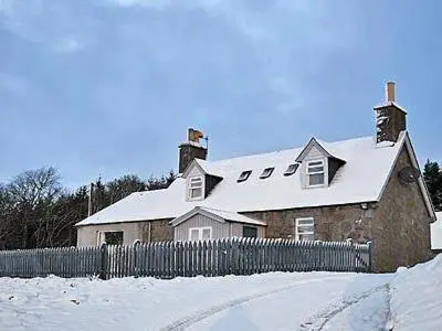 a house with a snow covered roof with a fence at Reid's Cottage in Lairg