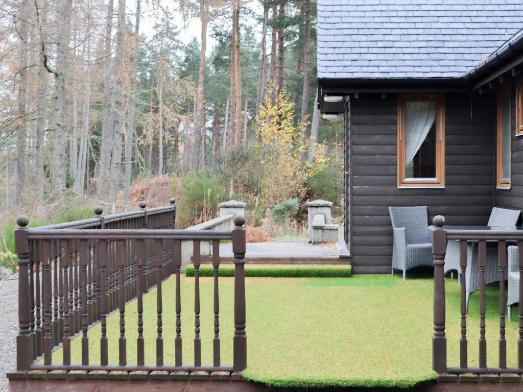 a house with a deck and a yard with grass at Park Lodge in Strachan