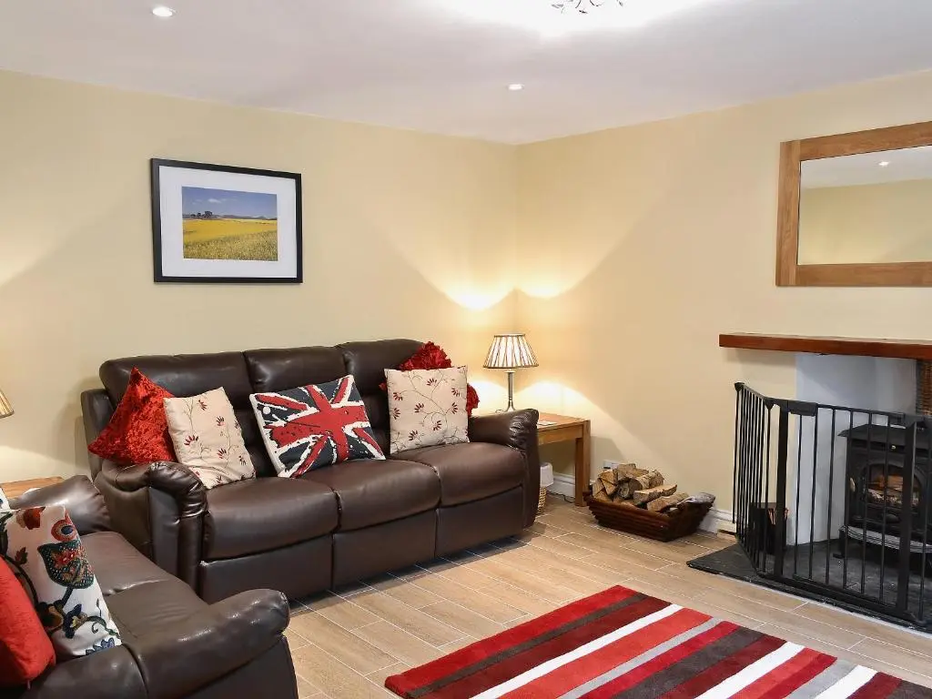 a living room with a leather couch and a fireplace at Longcroft Cottage - 28233 in Old Rayne