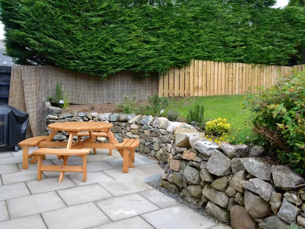 a wooden picnic table and a stone wall at Longcroft Cottage - 28233 in Old Rayne