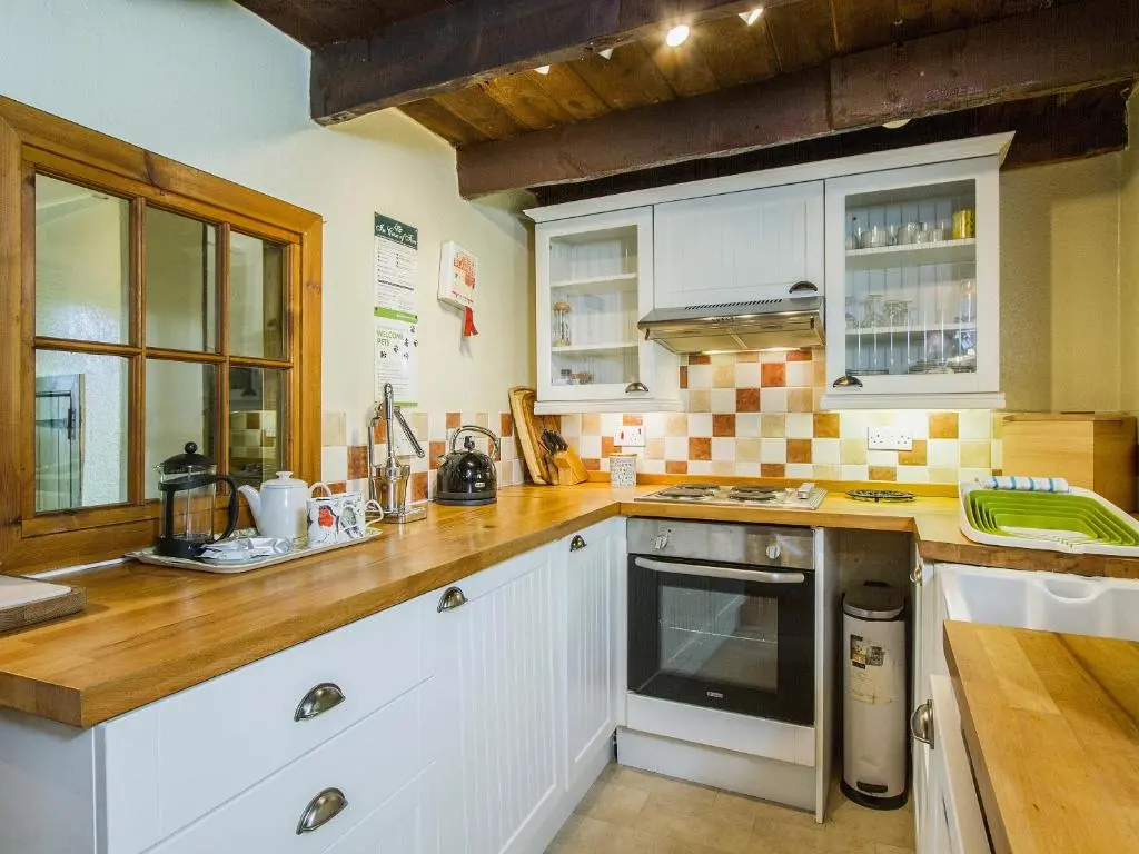 a kitchen with white cabinets and wooden counter tops at Gardener's Bothy in Balnaboth