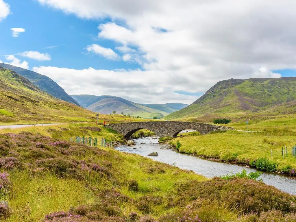 a stone bridge over a river in the hills at Glentairre Cottage - Swww in Balnaboth