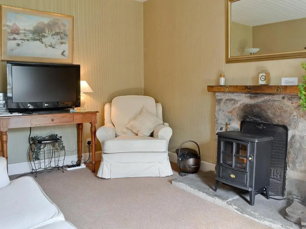 a living room with a fireplace and a chair and a television at Sunnyside in Kirkmichael