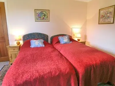 a bedroom with two beds with red covers and a chair at Dhuallow in Aberarder