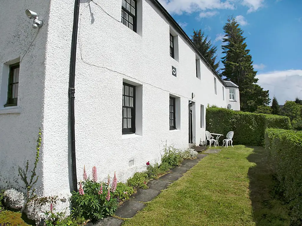 a white building with a garden and a table and chairs at Temple House West in Drumnadrochit