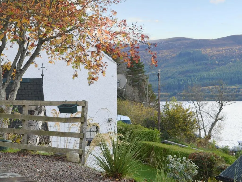 a fence next to a white building and a lake at Temple House West in Drumnadrochit