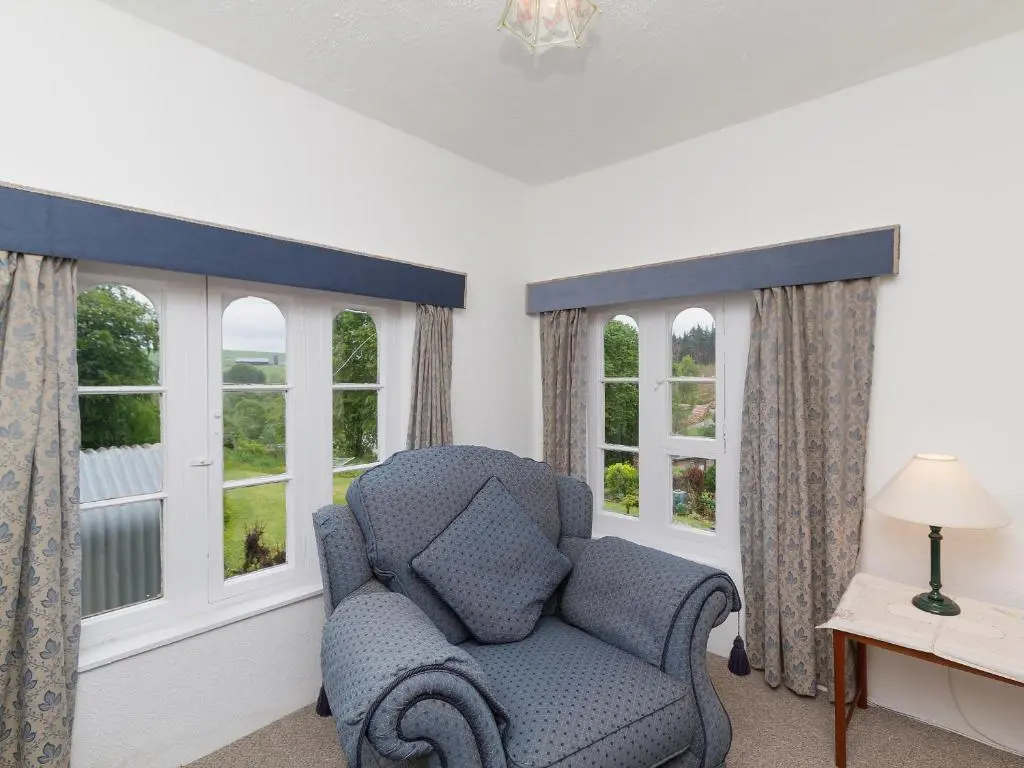 a living room with a chair and two windows at Symbister Suite in Turriff