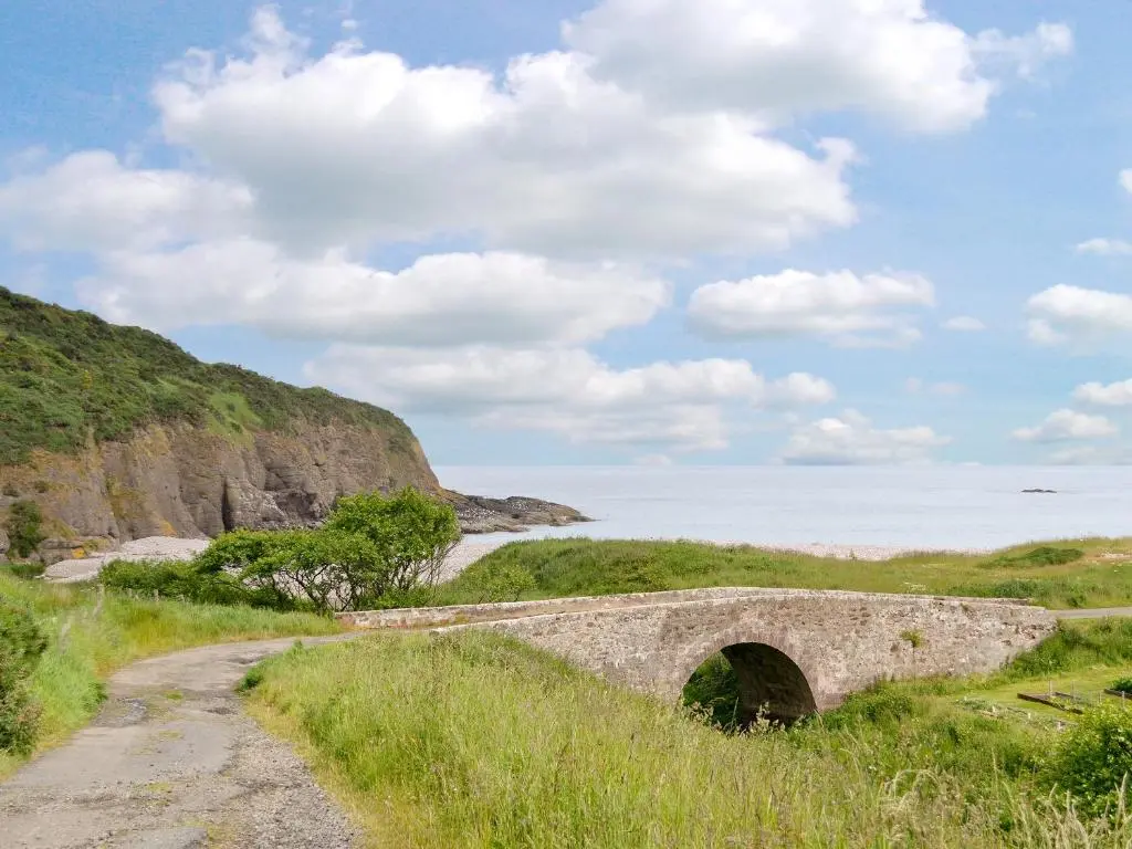 an old bridge over a dirt road near the beach at Mill Shore Cottage - 26817 in Pennan