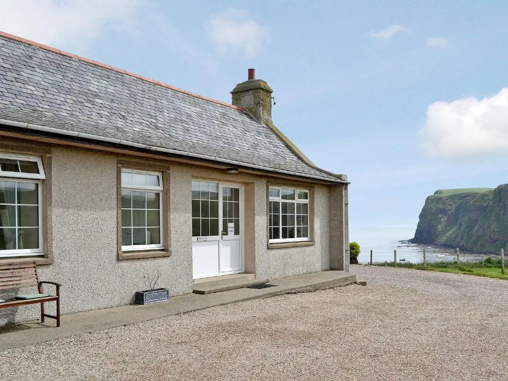 a house with a bench and a view of the ocean at Pennan Lodge - 26818 in Pennan