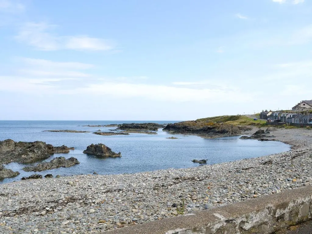 a beach with rocks in the water and houses at Scobach Lodge in Turriff