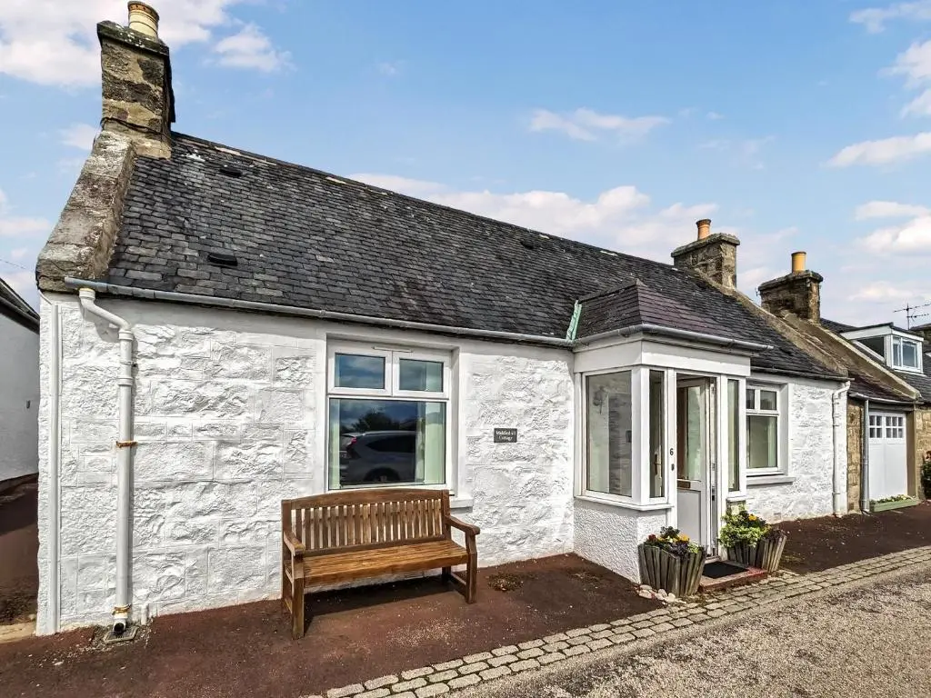 a white cottage with a bench in front of it at Middledrift Cottage in Brora
